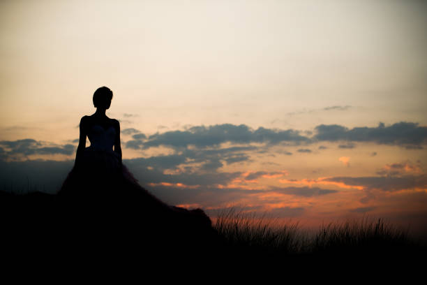 shot of a fairytale princess dark unrecognisable silhouette against a clear sky with a sunrise of a female in a ballgown or wedding dress.  victorian gown stock pictures, royalty-free photos & images