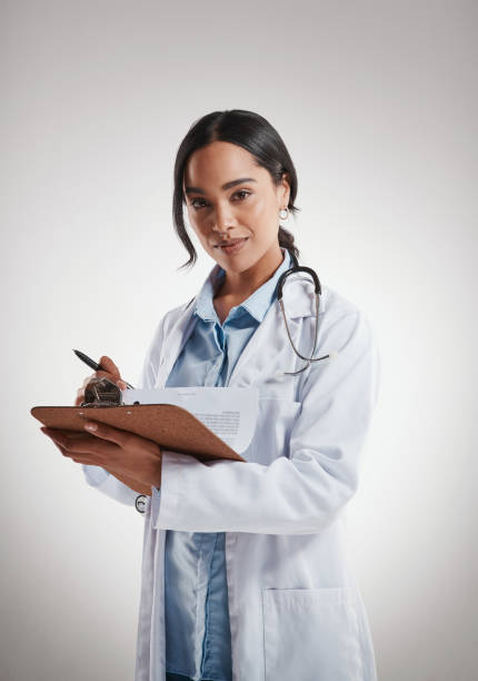 Shot of a female doctor holding a clipboard while standing against a grey background stock photo