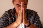 istock Shot of a handsome young man sitting alone at home and using his rosary during prayer 1323980776