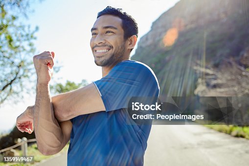 istock Shot of a handsome young man standing alone and stretching during his outdoor workout 1359149467
