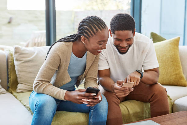Shot of a happy young couple using their smartphones on the sofa at home stock photo