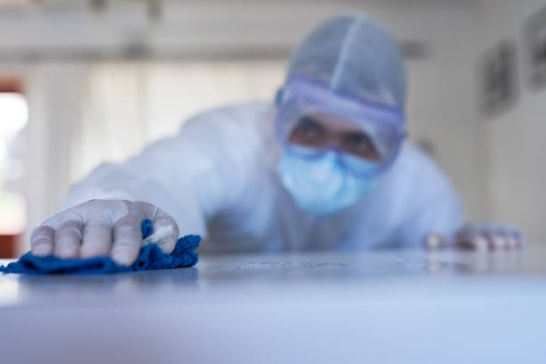 Shot of a man in a hazmat suit cleaning a surface in a house stock photo