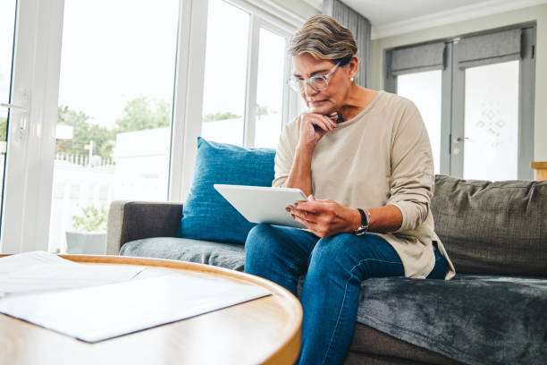 Shot of a mature woman using a digital tablet while going through paperwork at home stock photo