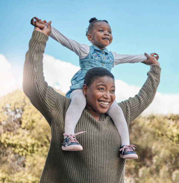 Shot of a mother carrying her daughter on her shoulders outdoors stock photo