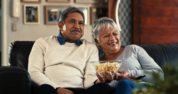 Shot of a senior couple watching tv on the sofa at home It's never too late to have romantic movie dates streaming service stock pictures, royalty-free photos & images
