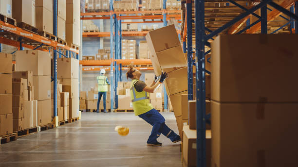 Shot of a Warehouse Worker Has Work Related Accident. He is Falling Down BeforeTrying to Pick Up Heavy Cardboard Box from the Shelf. Hard Injury at Work.  physical injury stock pictures, royalty-free photos & images