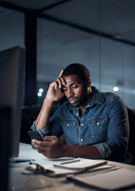 Shot of a young businessman looking stressed while using a smartphone during a late night in a modern office stock photo