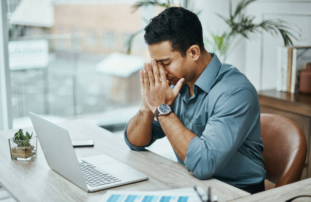 shot of a young businessman looking stressed while working in a modern office - stress work bildbanksfoton och bilder