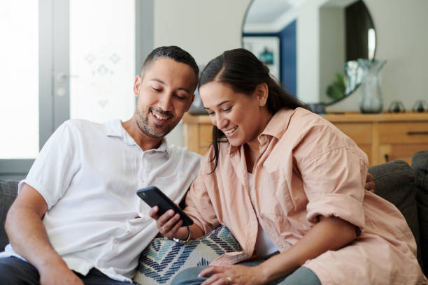 Shot of a young couple sitting on the sofa at home together and using a cellphone stock photo