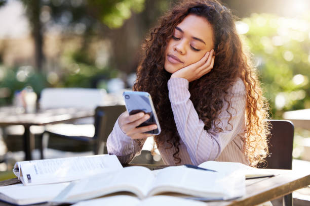 Shot of a young female student using a phone while studying at a cafe That seems like more fun Student planner apps stock pictures, royalty-free photos & images