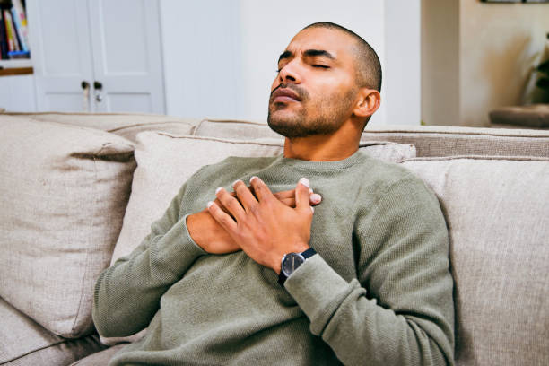 Shot of a young man experiencing chest pains at home stock photo
