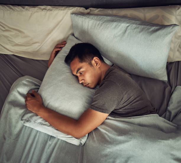 Shot of a young man lying in bed and looking unhappy at home stock photo