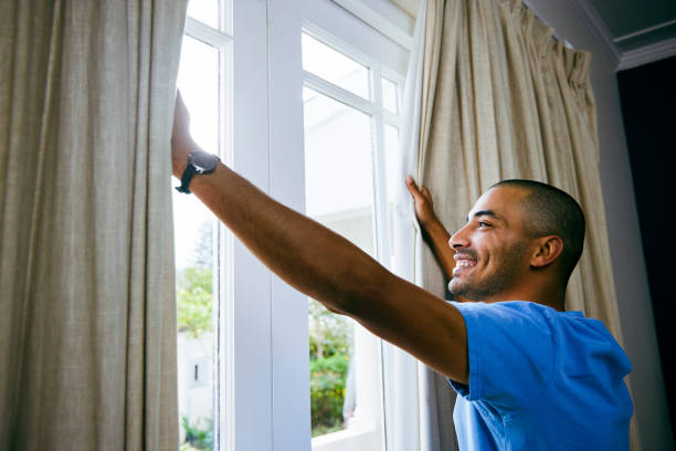 Shot of a young man opening up the curtains in a bedroom at home stock photo