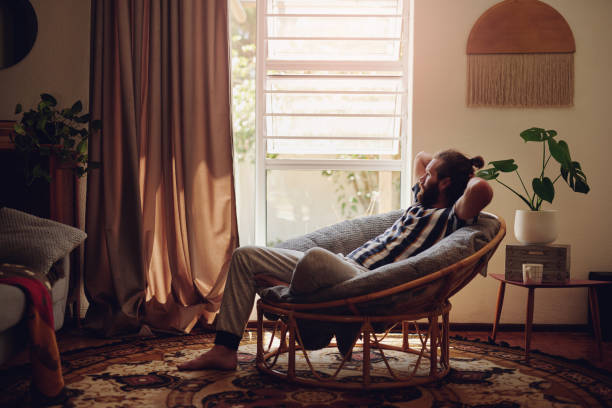 shot of a young man relaxing on a chair at home - lazer imagens e fotografias de stock