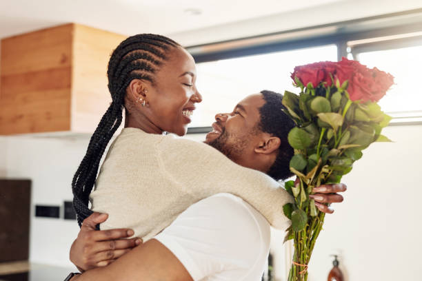 Shot of a young man surprising his wife with a bunch of flowers at home stock photo
