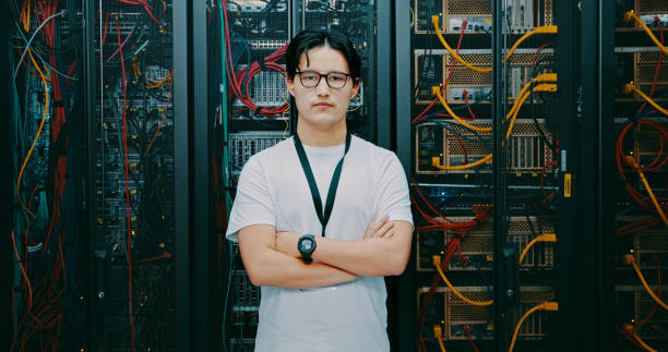 Shot of a young man using earphones while working in a server room stock photo