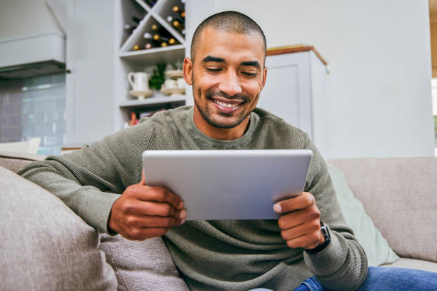 Shot of a young man using his digital tablet at home Entertainment in the palm of my hand streaming service stock pictures, royalty-free photos & images