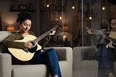 istock shot of a young woman playing guitar sitting on sofa near glass window at home:- stock photo 1312048883