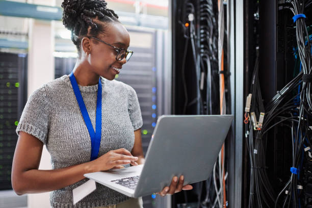 Shot of a young woman using a laptop in a server room stock photo
