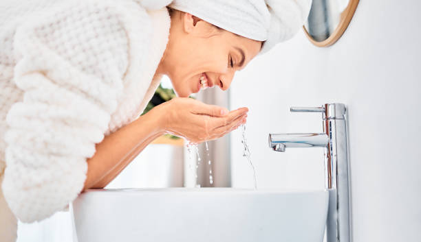Shot of a young woman washing her face in her bathroom stock photo