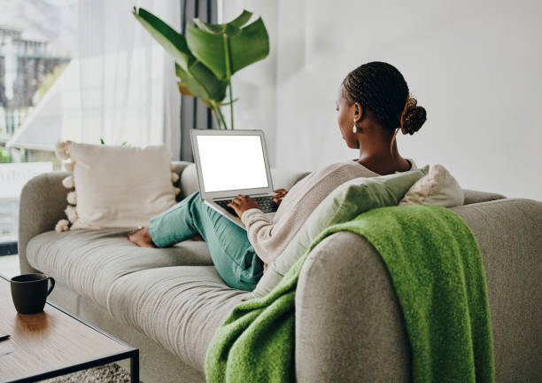 foto de una mujer joven trabajando en su computadora portátil en el sofá de su casa - bloguear fotos fotografías e imágenes de stock