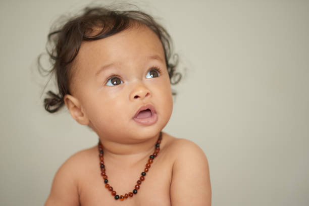 Shot of an adorable baby girl wearing a teething necklace at home stock photo