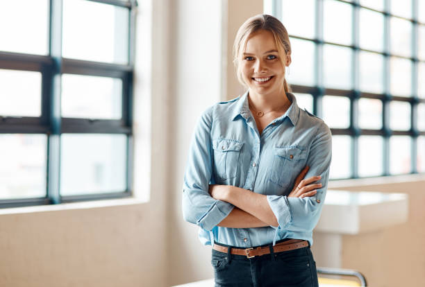 Shot of an attractive young businesswoman standing alone in the office with her arms folded during the day stock photo