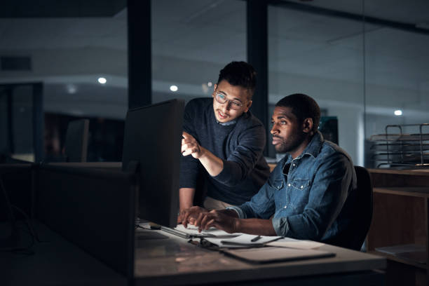 Shot of two young businessmen using a computer during a late night in a modern office stock photo
