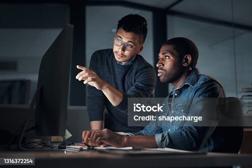 istock Shot of two young businessmen using a computer during a late night in a modern office 1316372254