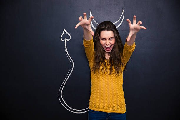Shouting woman pretending devil standing over chalkboard Shouting young woman with raised hands pretending devil standing over chalkboard background ugly skinny women stock pictures, royalty-free photos & images