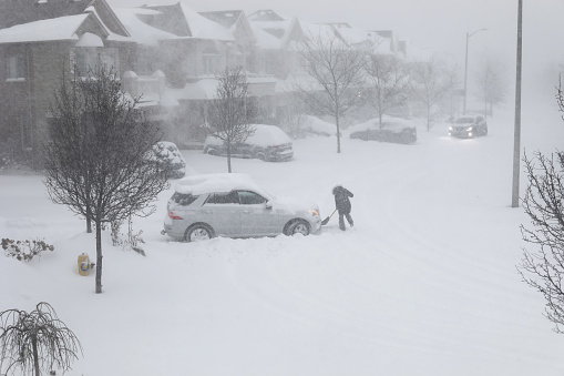 January 17, 2022 - Thornhill, Ontario, Canada: Lady is shoveling snow near the car stuck in snow trying to get out of it on January 17, 2022 in Thornhill, Ontario, Canada, when the huge snowstorm happened in and near Toronto area. Plowing snow from under the stuck in snow car.