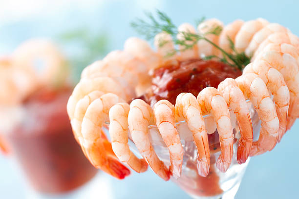Shrimp cocktail closeup with blurred cocktail in background Shrimp cocktail in a martini glass with cocktail sauce and dill garnish. cocktail sauce stock pictures, royalty-free photos & images