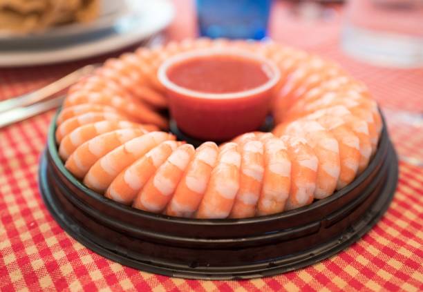 Shrimp Cocktail Ring of shrimp cocktail, with tails of large shrimp visible, with cocktail sauce in the middle, on a red and white tablecloth, March 31, 2017 cocktail sauce stock pictures, royalty-free photos & images