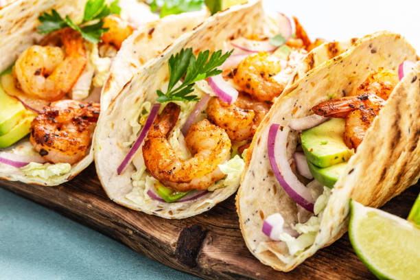Shrimp tacos. Seafood fajitas with cabbage, onion, parsley in tortillas served on wooden cutting board stock photo