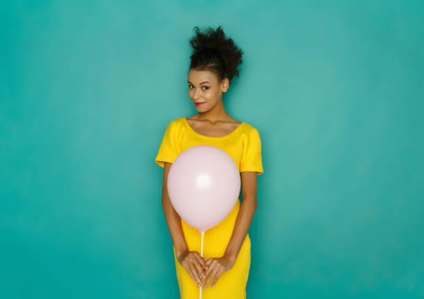Shy girl with balloon at studio background Shy girl with balloon. Smiling woman in bright yellow dress at azur studio background, copy space shy photos stock pictures, royalty-free photos & images