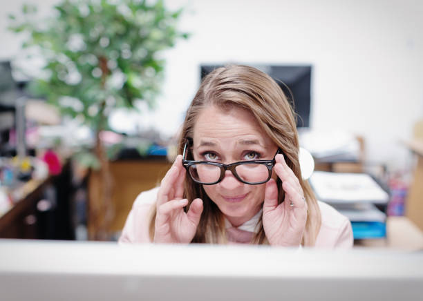 Shy office worker looks at you over her horn-rimmed spectacles stock photo