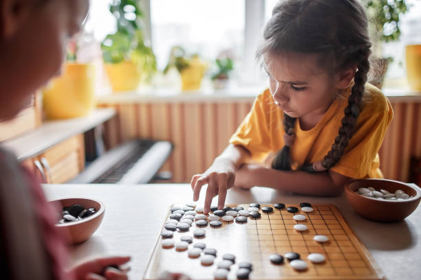 Sibling have fun together playing chess go at home, traditional Chinese board game, digital detox stock photo