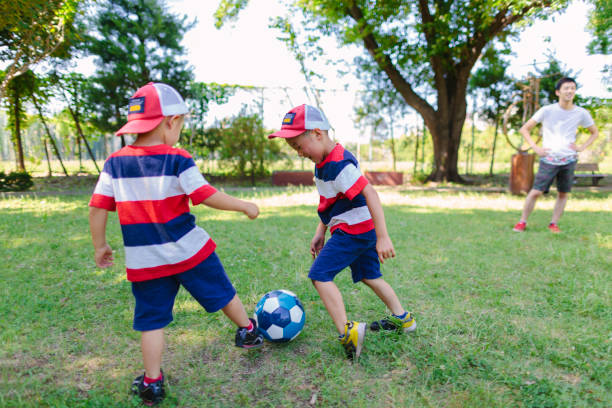 братья и сестры играют в футбол в общественном парке - july 4 стоковые фото и изображения