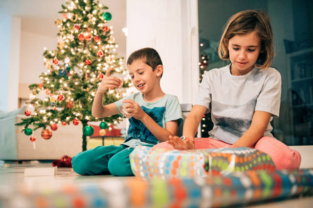 Siblings wrapping presents together Siblings wrapping presents by a Christmas tree hot mexican girls stock pictures, royalty-free photos & images