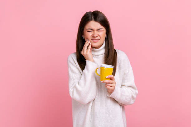 Sick brunette woman suffering from sensitive teeth after drinking hot or cold beverage, cavities. stock photo