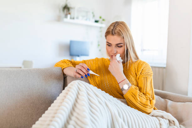 Sick desperate woman has coronavirus. Covid 19 , cold, sickness, allergy concept. Pretty sick woman has runnning nose, rubs nose with handkerchief and looking at temperature on thermometer stock photo