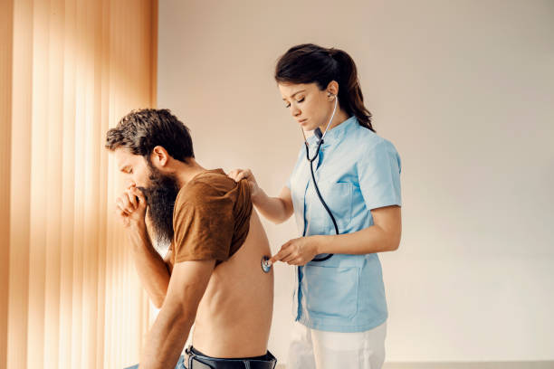 A sick man at doctor's office coughing while a female doctor examining his lungs. Medical service, disease prevention and healing. stock photo