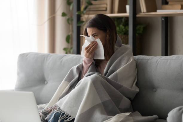 Sick woman covered with plaid blowing nose on paper tissue Sick young woman sitting on couch at home, unhealthy girl covered with warm plaid sneezing blowing her nose on paper tissue suffering from grippe temperature or seasonal allergy, cold dwelling concept flu stock pictures, royalty-free photos & images