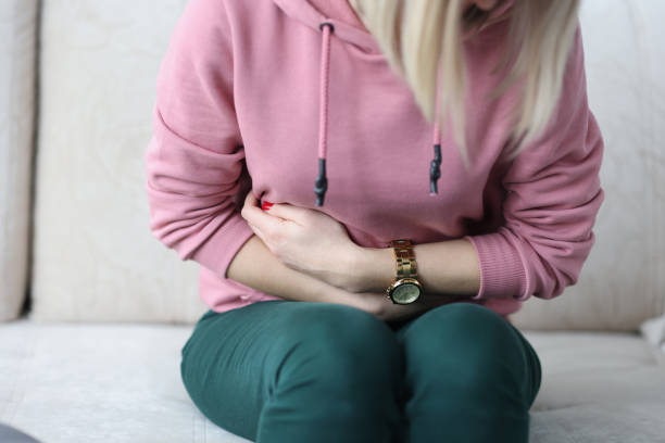 Sick woman siting on couch and holding her stomach with her hands closeup stock photo