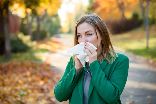 Sick young woman with cold and flu standing outdoors, sneezing,...
