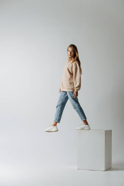 Side image of a teenage girl walking of a white cube, stepping into the air stock photo