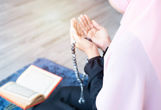 lato della giovane asiatica bella donna musulmana pregare con perline e leggere corano sedersi sul tappeto mat con meditazione in moschea. - salah foto e immagini stock