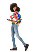 Full body side portrait of happy young black woman walking with cellphone and book bag