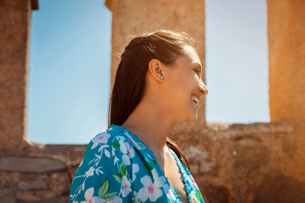 side profile photo of a young woman in a summer dress enjoying warm sunlight stock photo