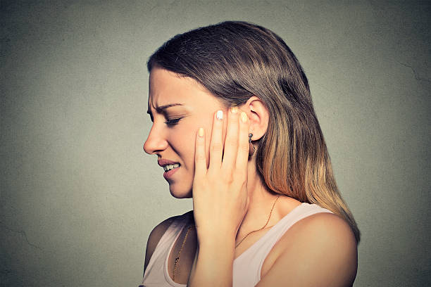 side profile sick young woman having ear pain Tinnitus. Closeup side profile sick young woman having ear pain touching her painful head isolated on blue background human ear stock pictures, royalty-free photos & images